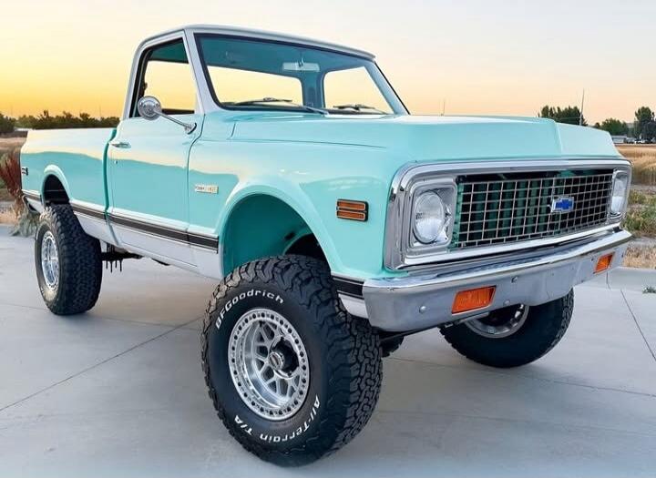 A vintage light-blue Chevrolet pickup truck with oversized off-road tires and lifted suspension, chrome grille, and two-tone body.
