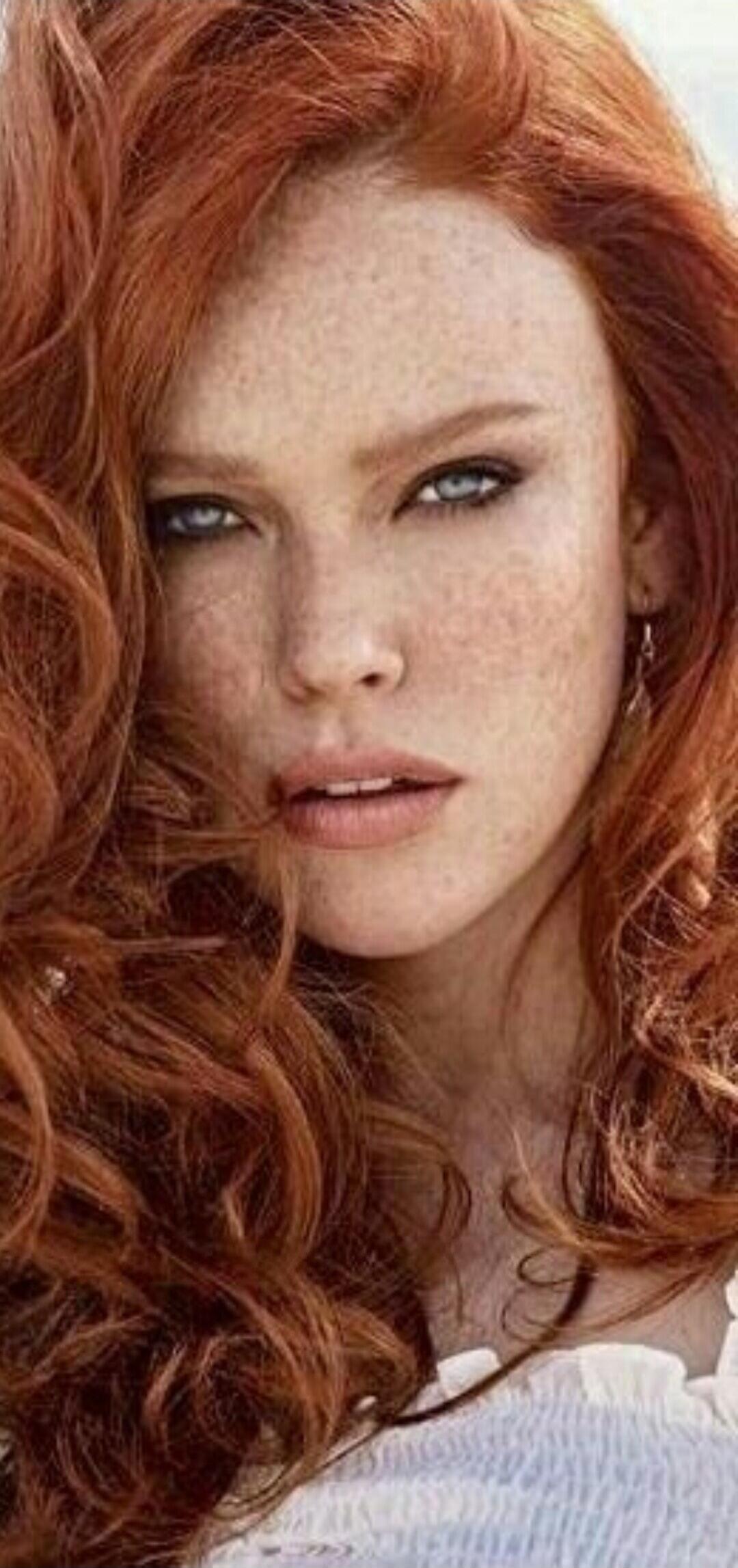 A close-up portrait of a woman with red curly hair and freckles.