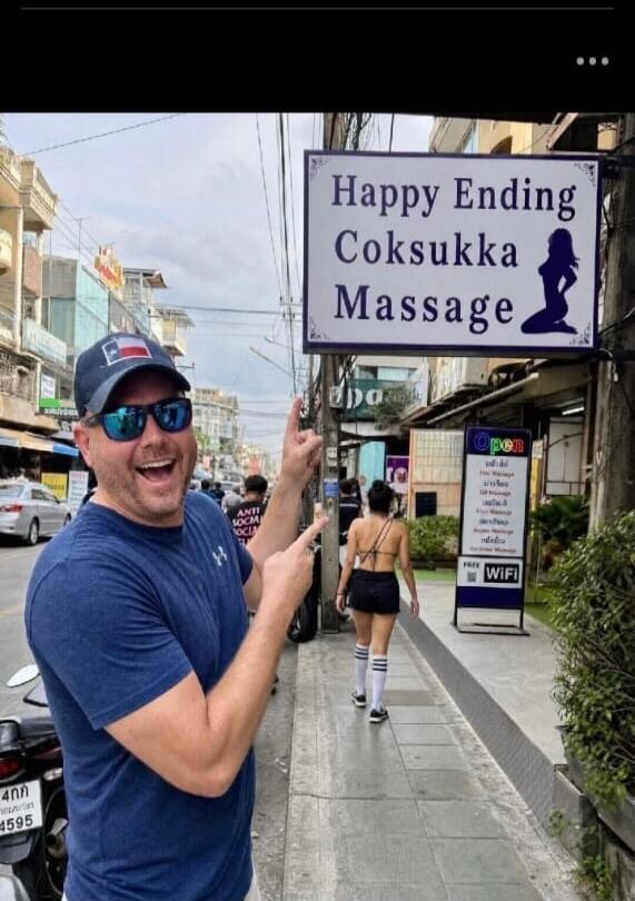 A man in a cap and sunglasses points excitedly at a sign that reads 