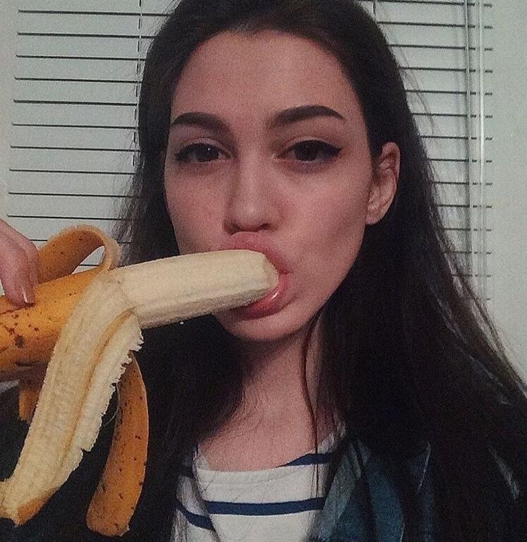 A woman is biting a peeled banana.