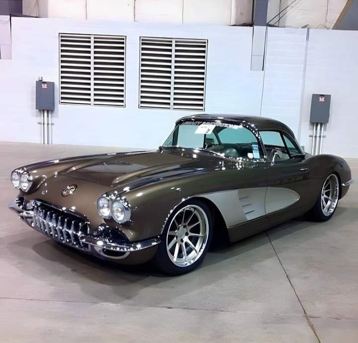 A classic Chevrolet Corvette, likely a C1 generation, with custom bronze paint and silver side coves, parked indoors. Text on windshield: LEGACY RESTORATION.