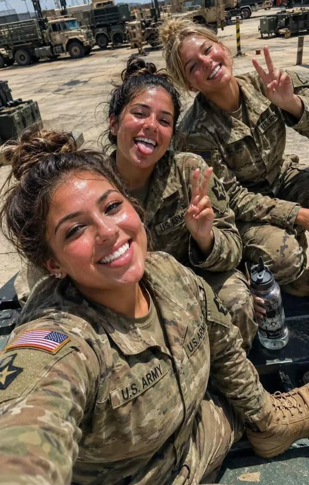 Three women in U.S. Army camouflage uniforms are smiling and posing for a selfie. One woman in the middle is sticking out her tongue, and another on the right is making a peace sign. The woman in the foreground is smiling broadly. The text 'U.S. ARMY' is visible on their uniforms.
