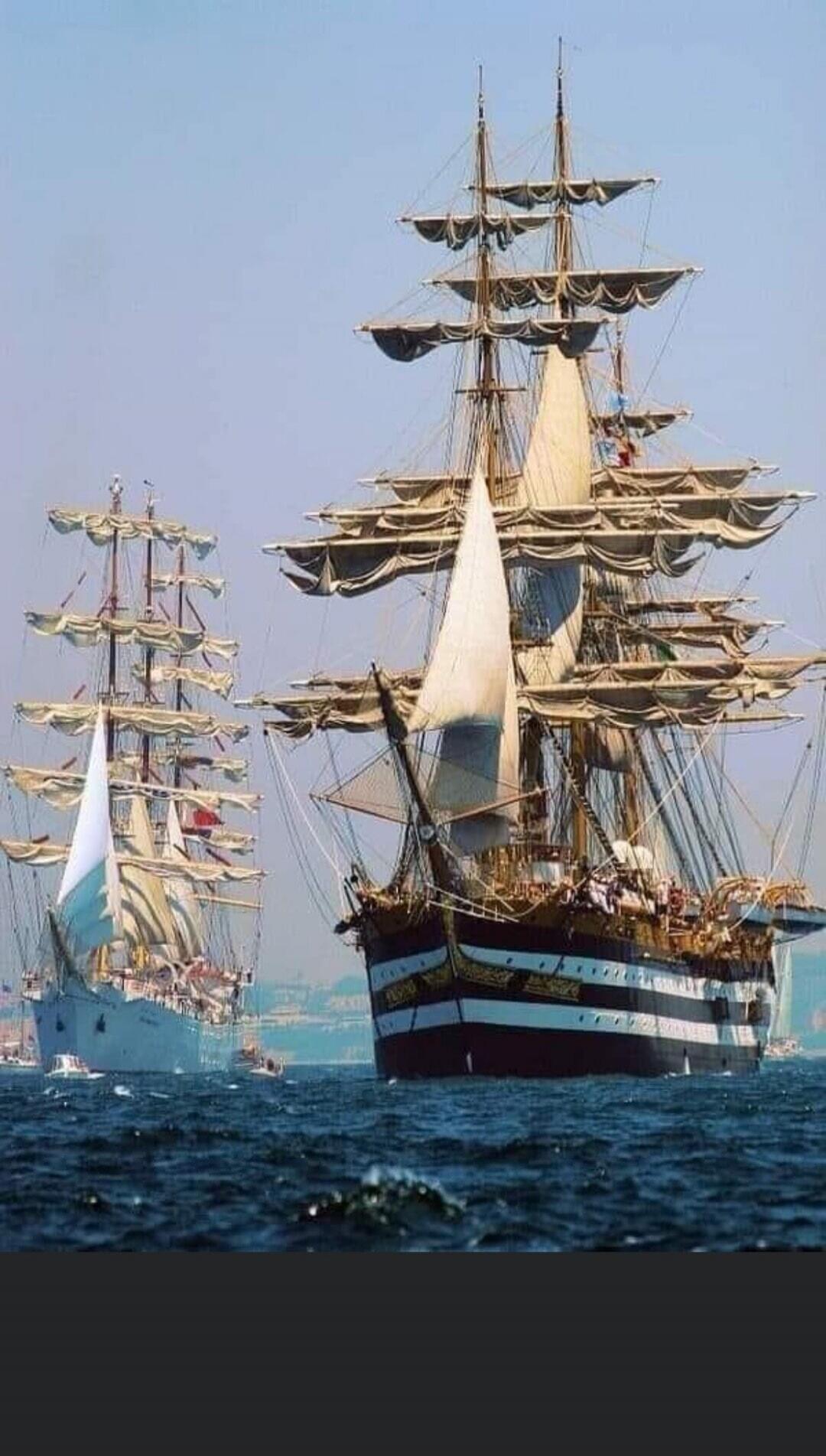 Two tall sailing ships with multiple masts and full sails on the open sea.