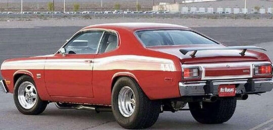 Red classic muscle car from the 1970s photographed from the side/rear on an open area.