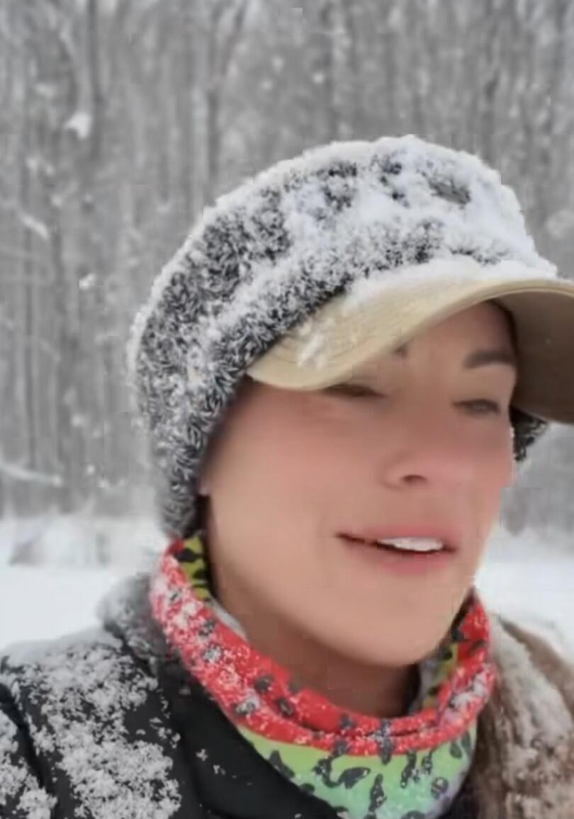 A woman in a winter hat and scarf, covered in snow.