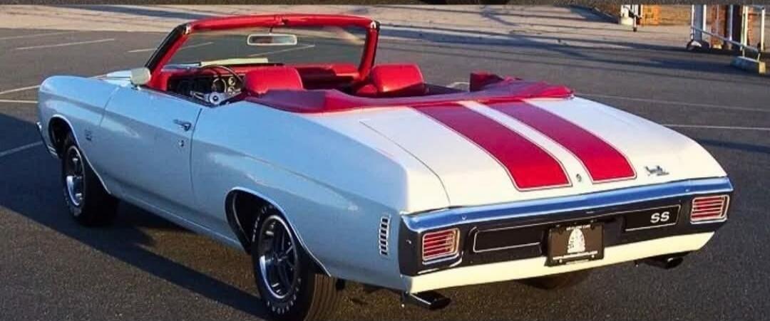 A classic white convertible car with red racing stripes and a red interior, parked on asphalt. The car has 'SS' badging on the rear.