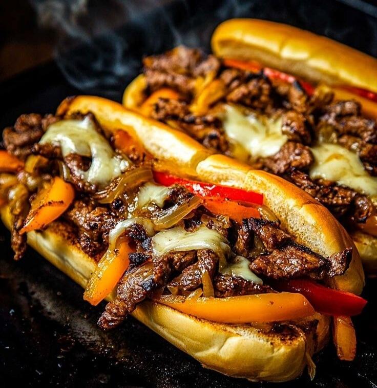 Beef sandwich with peppers and onions and melted cheese on soft sub rolls. Smoky, grilled beef strips tucked into hot dog-style buns with orange and red bell peppers and melted cheese slices.