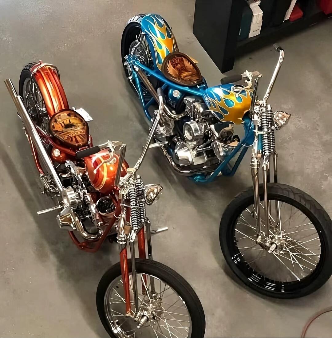 Two custom motorcycles with flame paint jobs, one orange/red and one blue/yellow, parked indoors on a concrete floor.