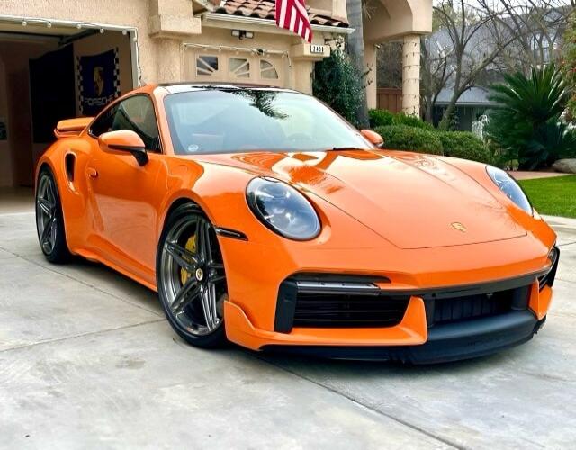 Orange Porsche 911 sports car parked in a driveway.
