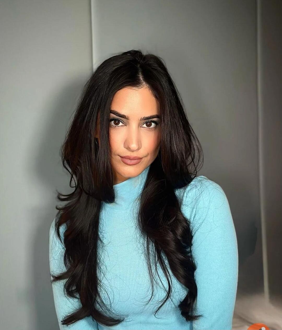 A portrait of a woman with long dark hair wearing a light blue turtleneck sweater.