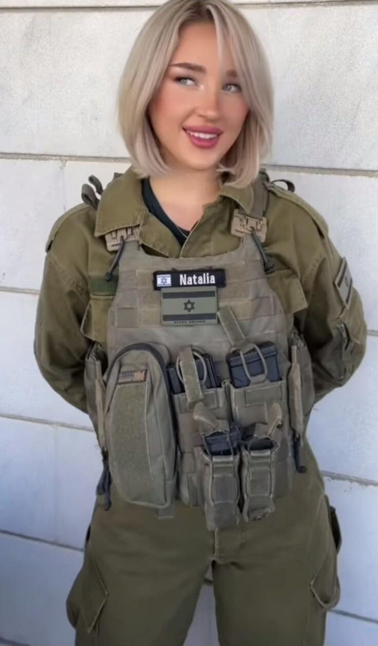 A woman wearing a military uniform and tactical vest with a name patch 'Natalia' and an Israeli flag patch.