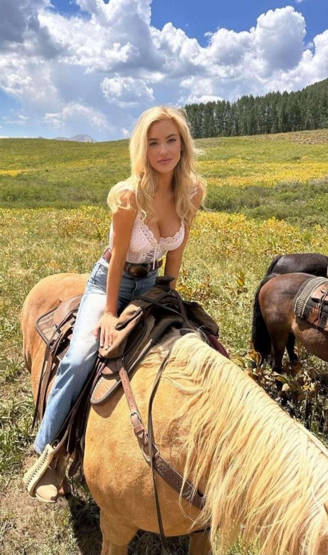 Photo of a blonde woman riding a horse in a field.