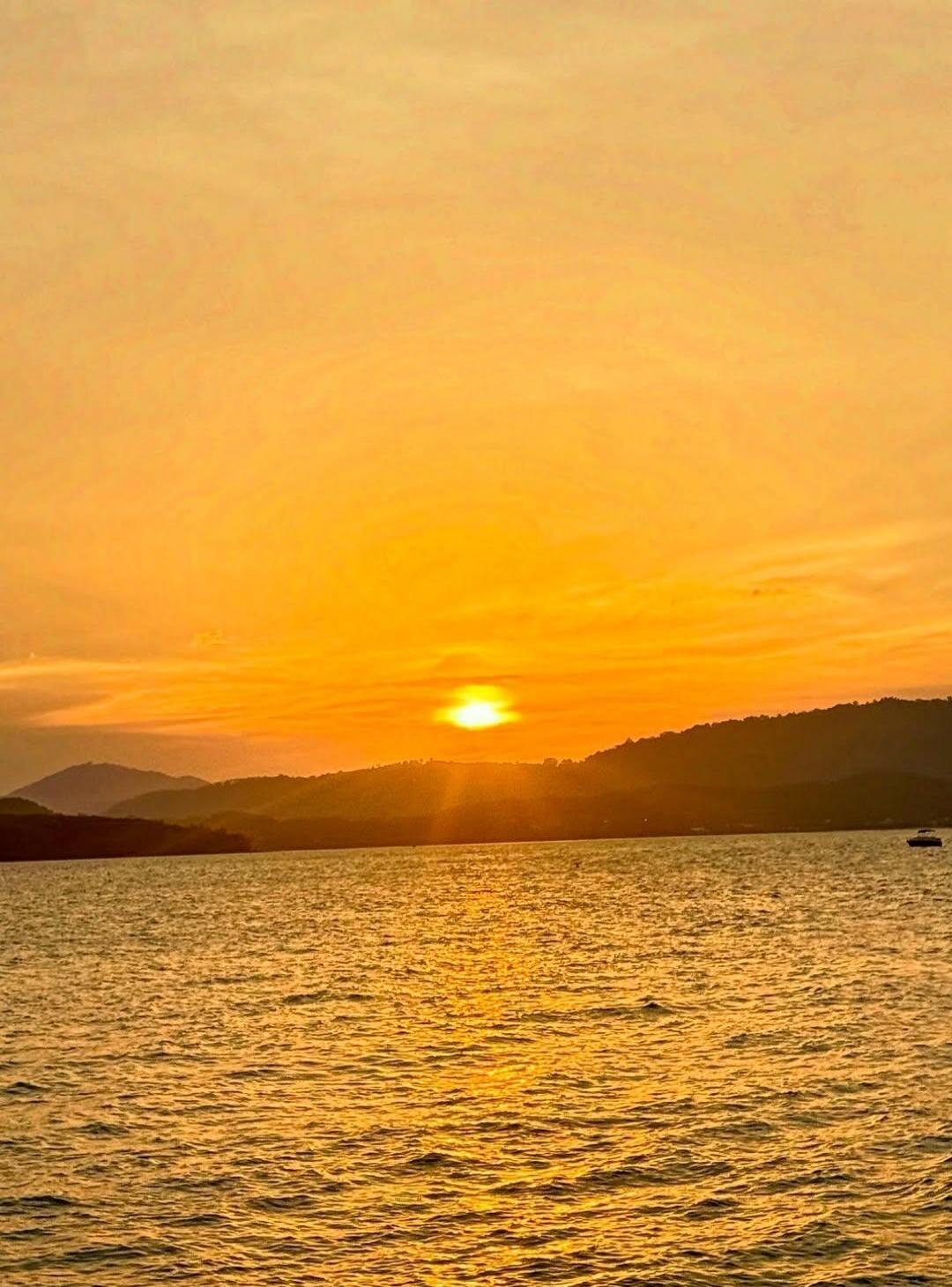Sunset over the water with mountains in the background and a boat on the right.