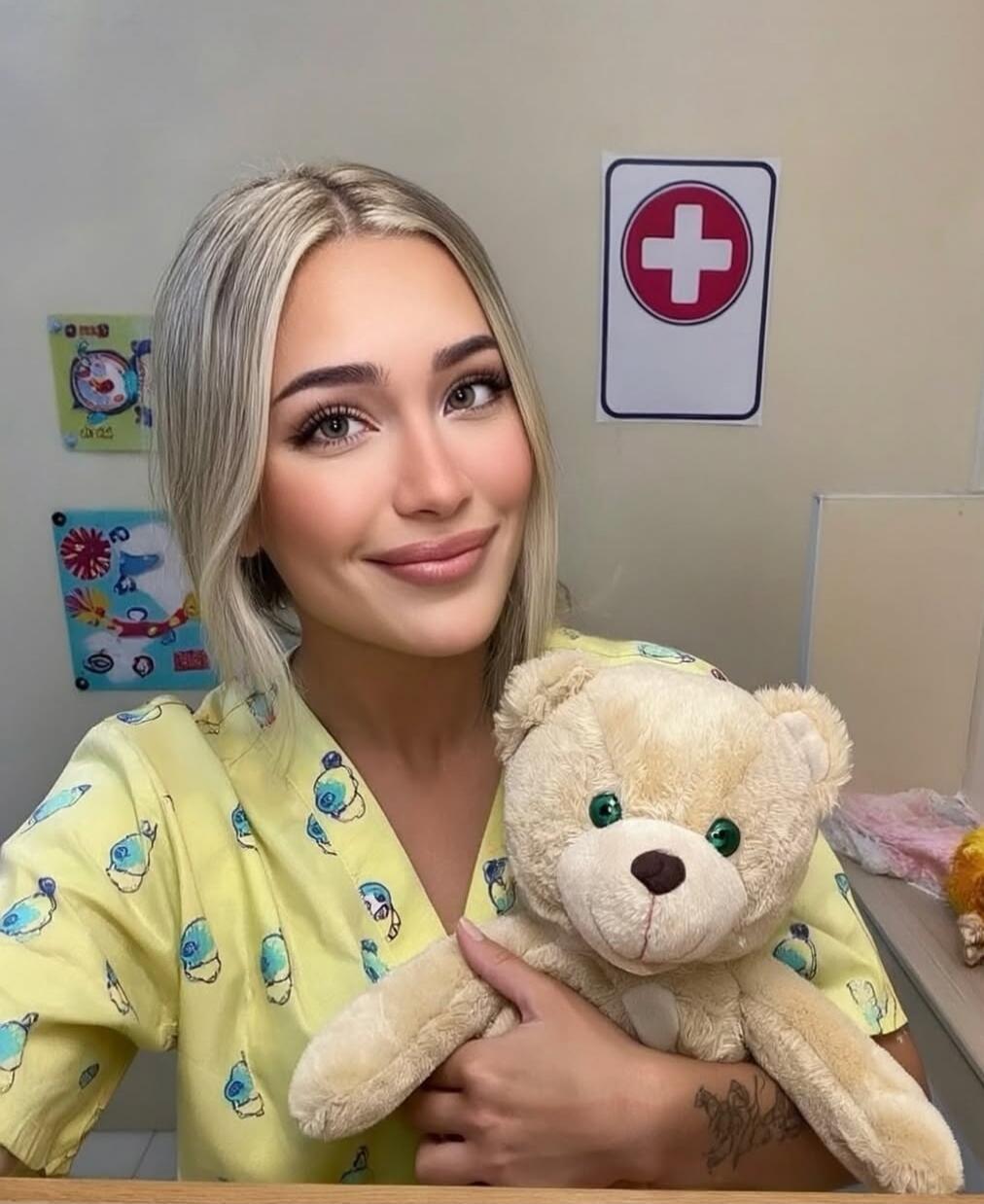 A woman in yellow medical scrubs holding a teddy bear.