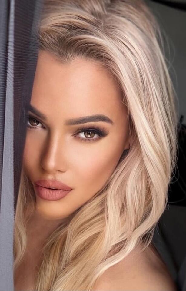 Close-up portrait of a blonde woman with makeup, looking at the camera.