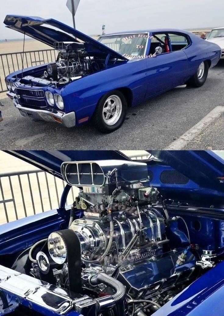 Hot Rod To Pro-Mods. A powerful blue classic muscle car, possibly a Chevrolet Chevelle, with its hood open, showcasing a highly polished and supercharged engine. The car is parked outdoors, likely at a car show or event.