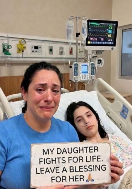 A crying woman holds a sign that reads: 'MY DAUGHTER FIGHTS FOR LIFE. LEAVE A BLESSING FOR HER 🙏'. Next to her, a young girl lies in a hospital bed with a nasal cannula, looking unwell. Hospital equipment is visible in the background.