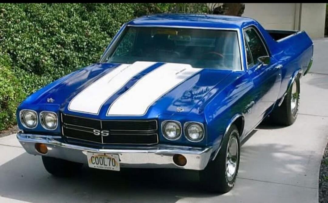 A classic blue Chevrolet El Camino SS from 1970 with white racing stripes. The license plate reads 'COOL70'. The car features the 'SS' emblem on its grille.