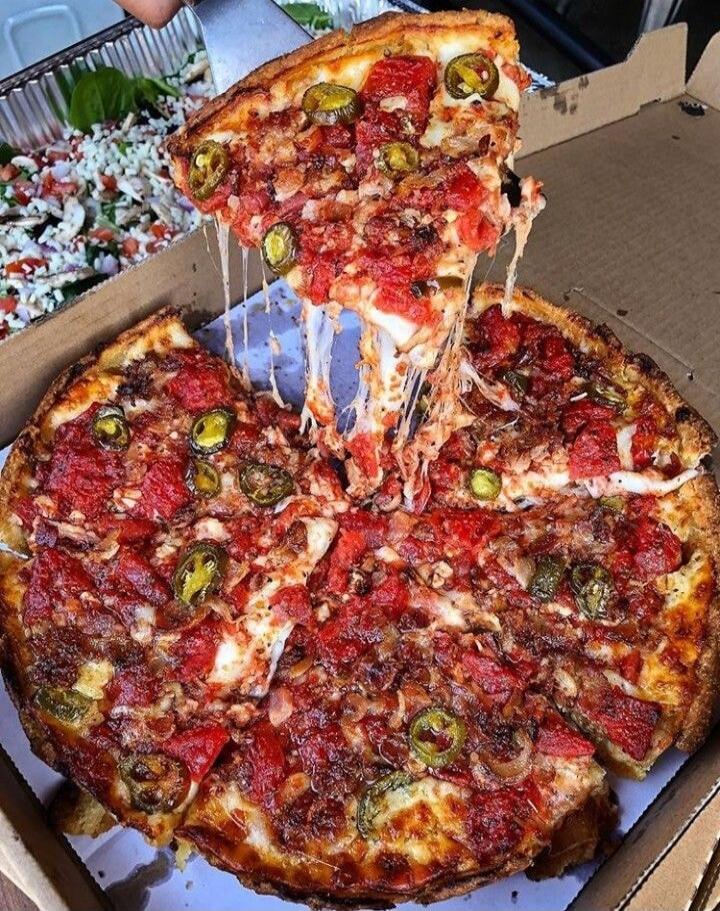 A slice of pizza is being lifted from a whole pizza, showing melted cheese stretching.