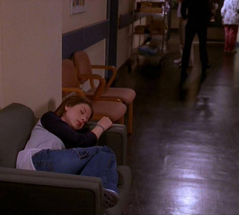 A girl sleeping on a couch in a hallway.