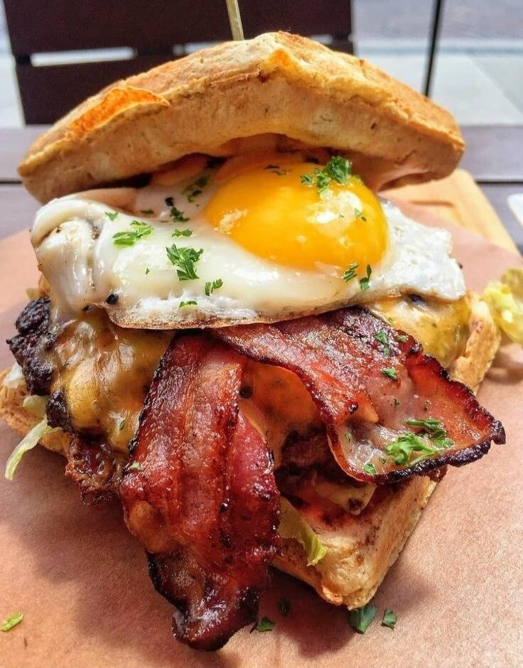 A bacon cheeseburger topped with a sunny-side-up egg inside a toasted bun.