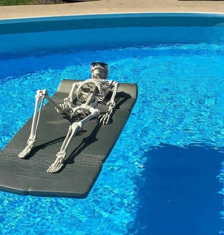 Skeleton lounging on a pool float in a blue swimming pool.