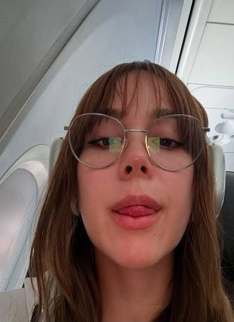 A person on an airplane making a playful face, sticking out their tongue and wearing round glasses.