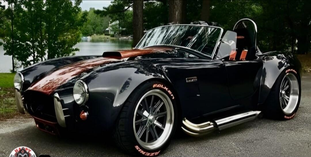Black Cobra-style convertible sports car with a red racing stripe down the center, chrome side pipes, and racing wheels.