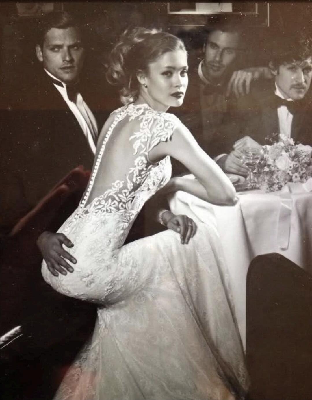 A vintage photo of a woman in a lace backless gown seated at a table with men in formal wear.