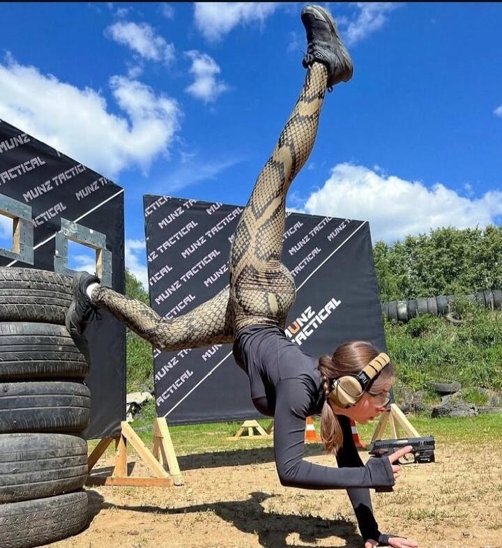 MUNZ TACTICAL. A woman performs an acrobatic handstand while holding a pistol at an outdoor tactical training facility.