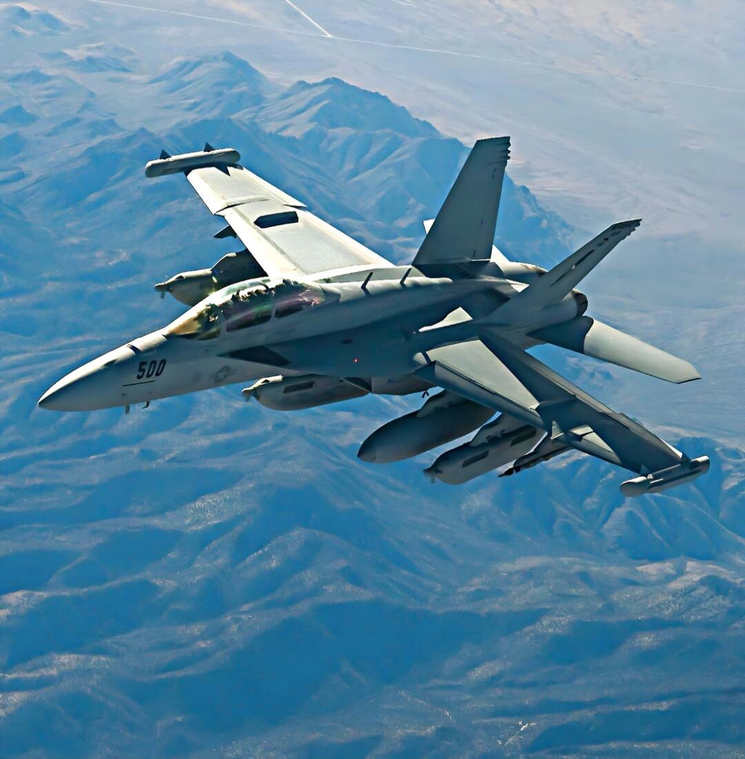A military fighter jet in flight over mountainous terrain.