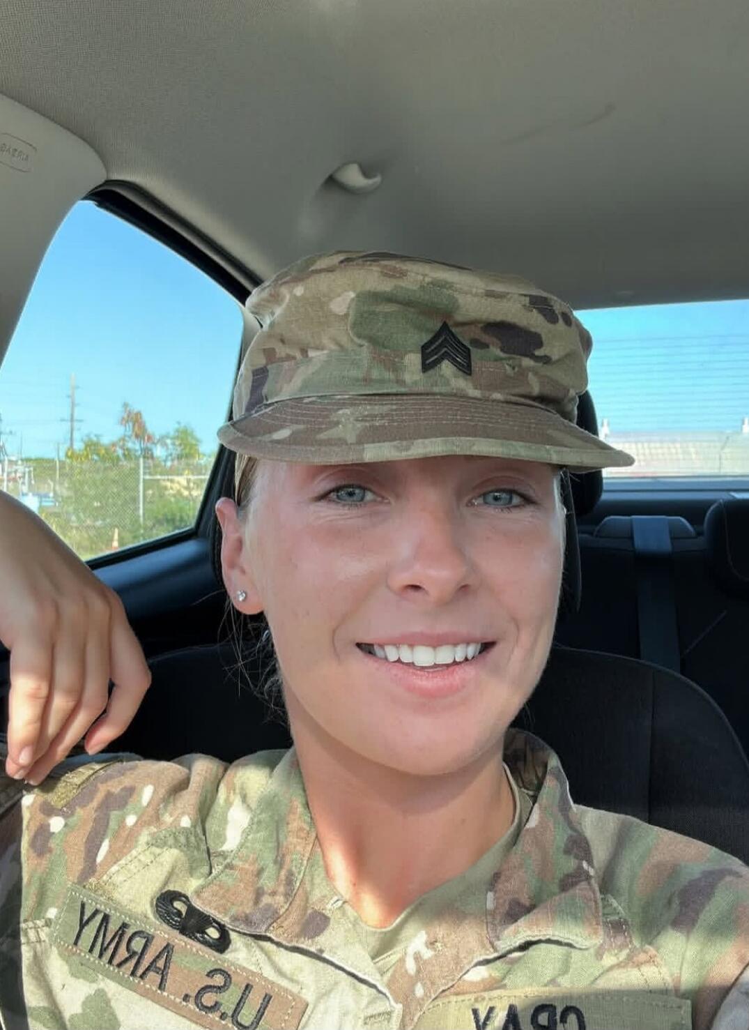 U.S. ARMY. A woman in a military uniform, wearing a camouflage patrol cap with Staff Sergeant rank insignia, is smiling while sitting in a car.