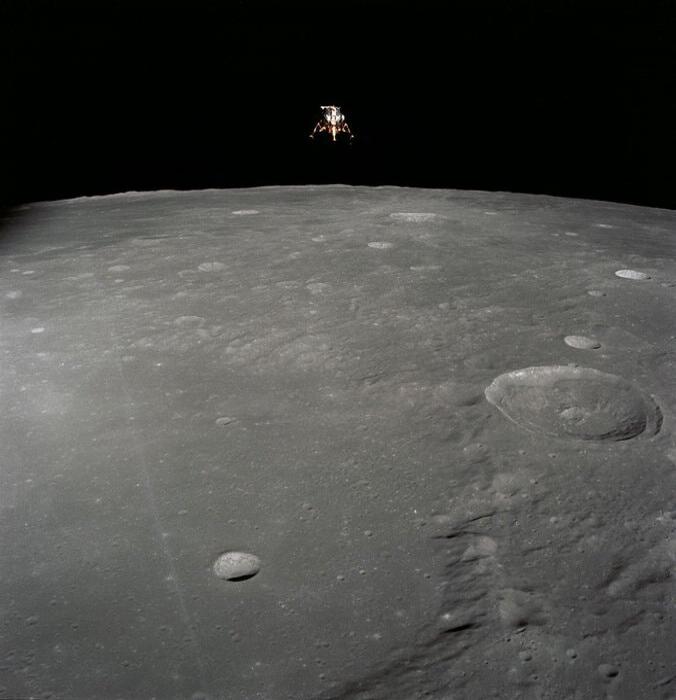 A lunar surface photograph with a distant lander or spacecraft above the horizon.