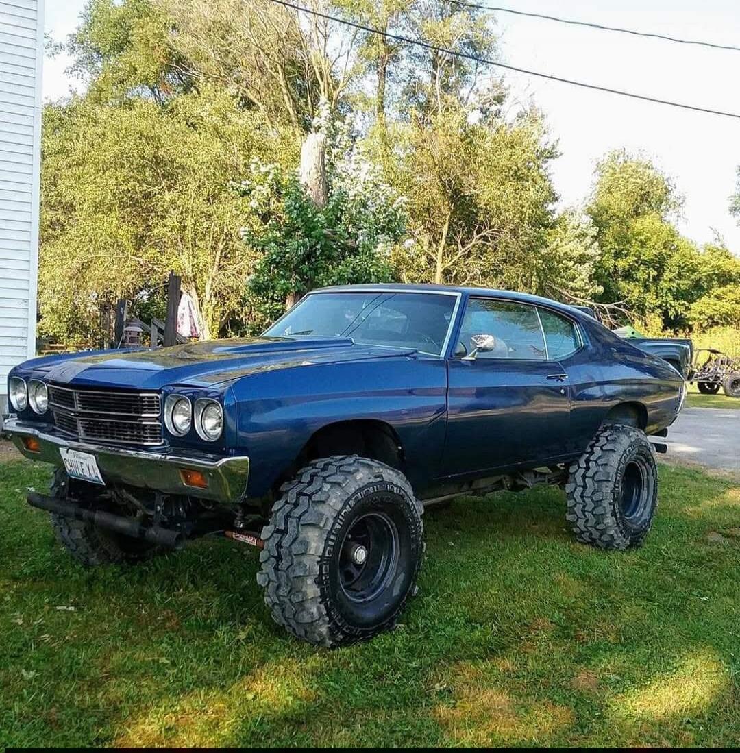 Blue classic muscle car with oversized off-road tires parked on grass.