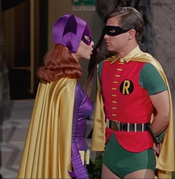 Batgirl and Robin cosplay from a 1960s-inspired Batman show sharing a close moment.
