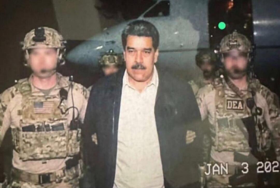 JAN 3 2021? (timestamp) A man in a light shirt and dark jacket is escorted by soldiers in tactical gear. The soldiers have patches reading 'DEA'.