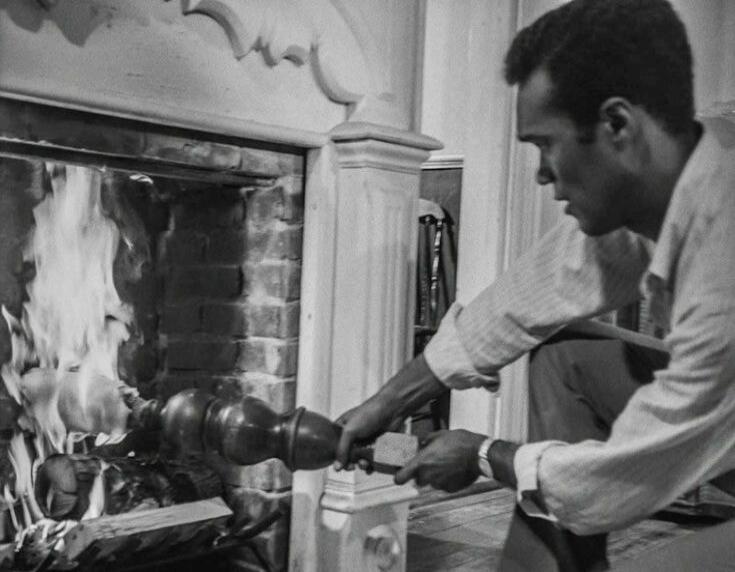 A man is holding a decorative wooden object near a burning fireplace.