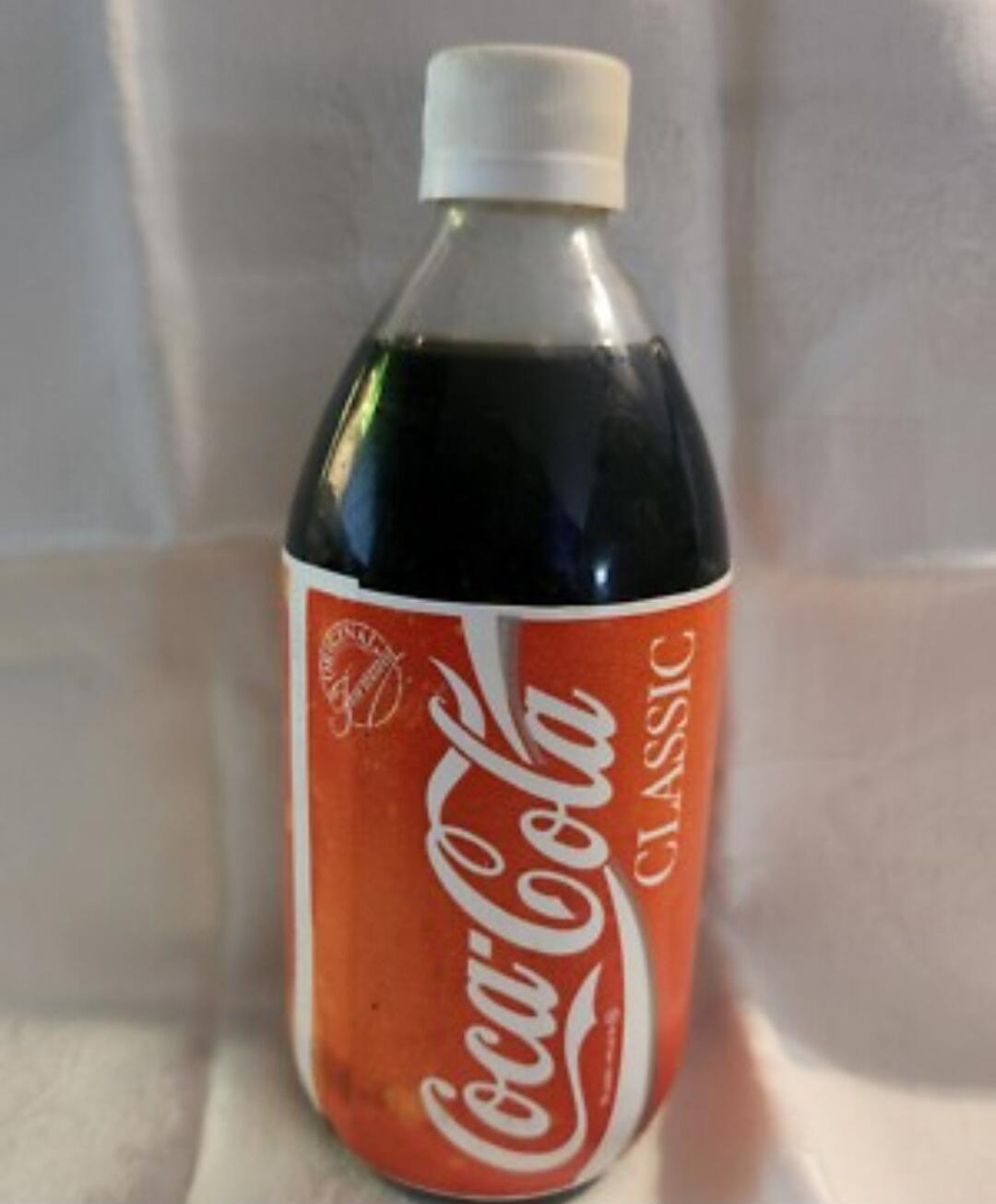 A bottle of Coca-Cola Classic with a white cap and an orange-red label, featuring the iconic Coca-Cola logo and 'CLASSIC' text.