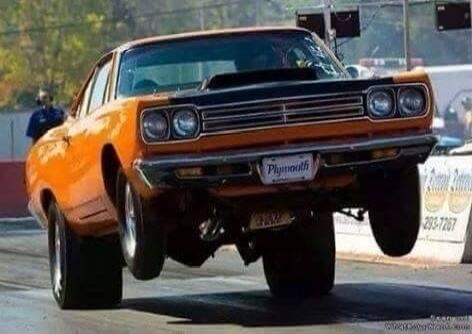 Orange classic car performing a wheelie stunt on the street.