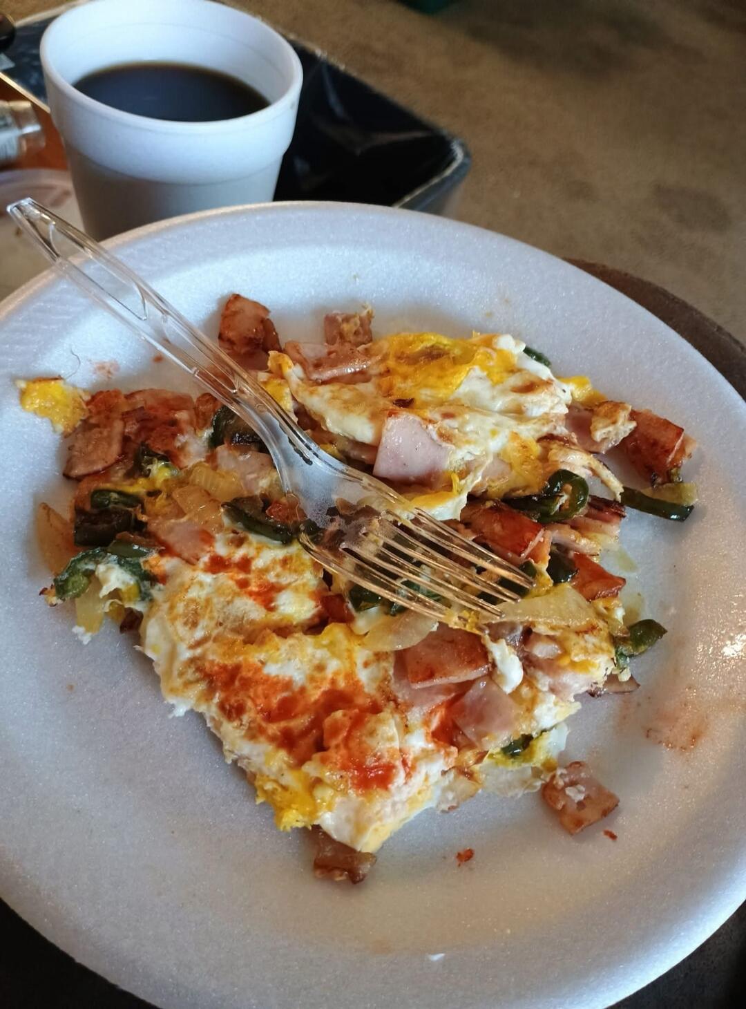 A breakfast plate with scrambled eggs, cheese, ham, and vegetables, with a cup of coffee in the background.