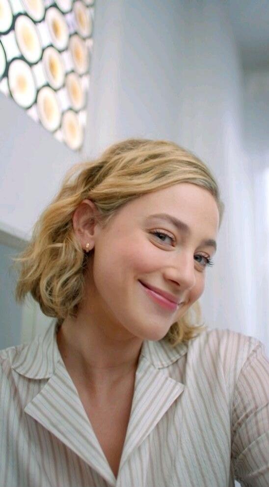 A smiling woman with short blonde hair wearing a light striped shirt.