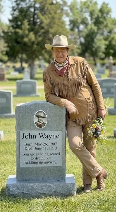 A man in a cowboy outfit is posing and leaning on a tombstone in a cemetery. The tombstone bears text with a name redacted, along with birth/death dates and a humorous epitaph: 'Courage is being scared to death, but saddling up anyway.'