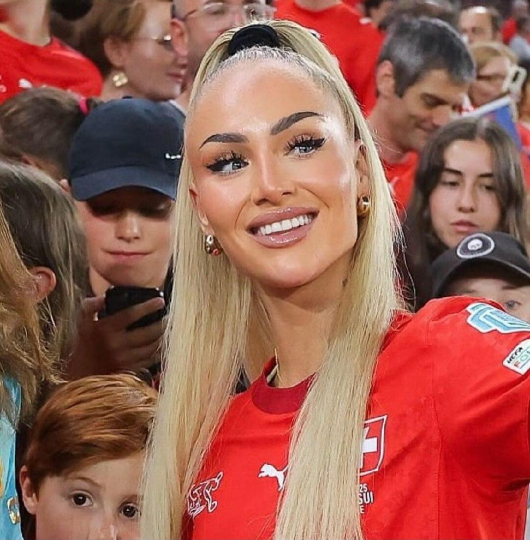 A blonde woman in a red sports jersey posing for a photo among a crowd.