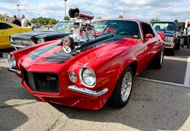 Red vintage Chevrolet muscle car with a large exposed supercharger blower on the hood, parked at a car show.