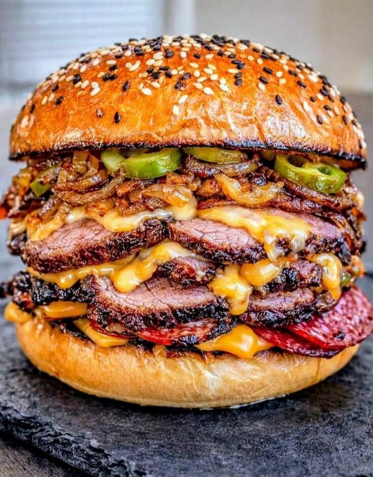 A large appetizing burger with thick slices of meat, melted cheese, and pickles.