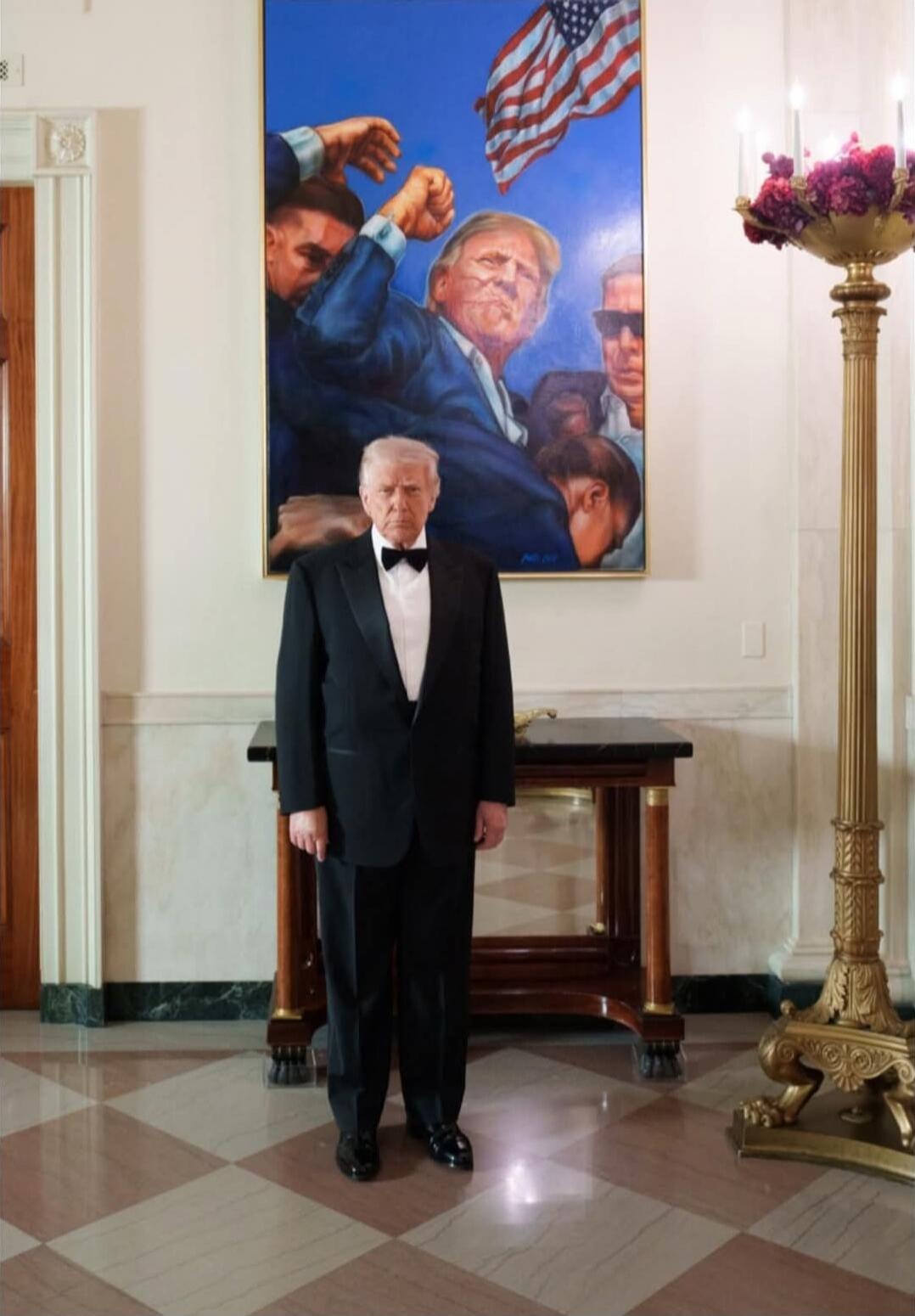 A man in a black tuxedo standing indoors in front of a painting.