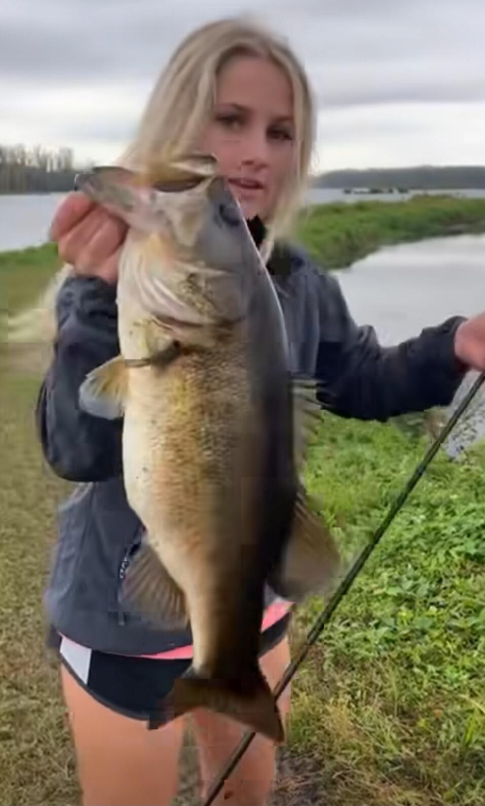 A person holding a large fish near a riverbank.