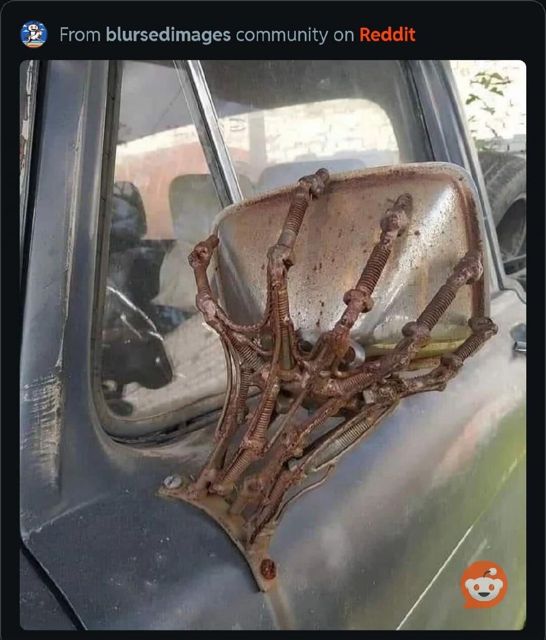 From blursedimages community on Reddit. A rusty, skeletal, hand-shaped side mirror attached to an old car, giving it a unique and somewhat eerie appearance.