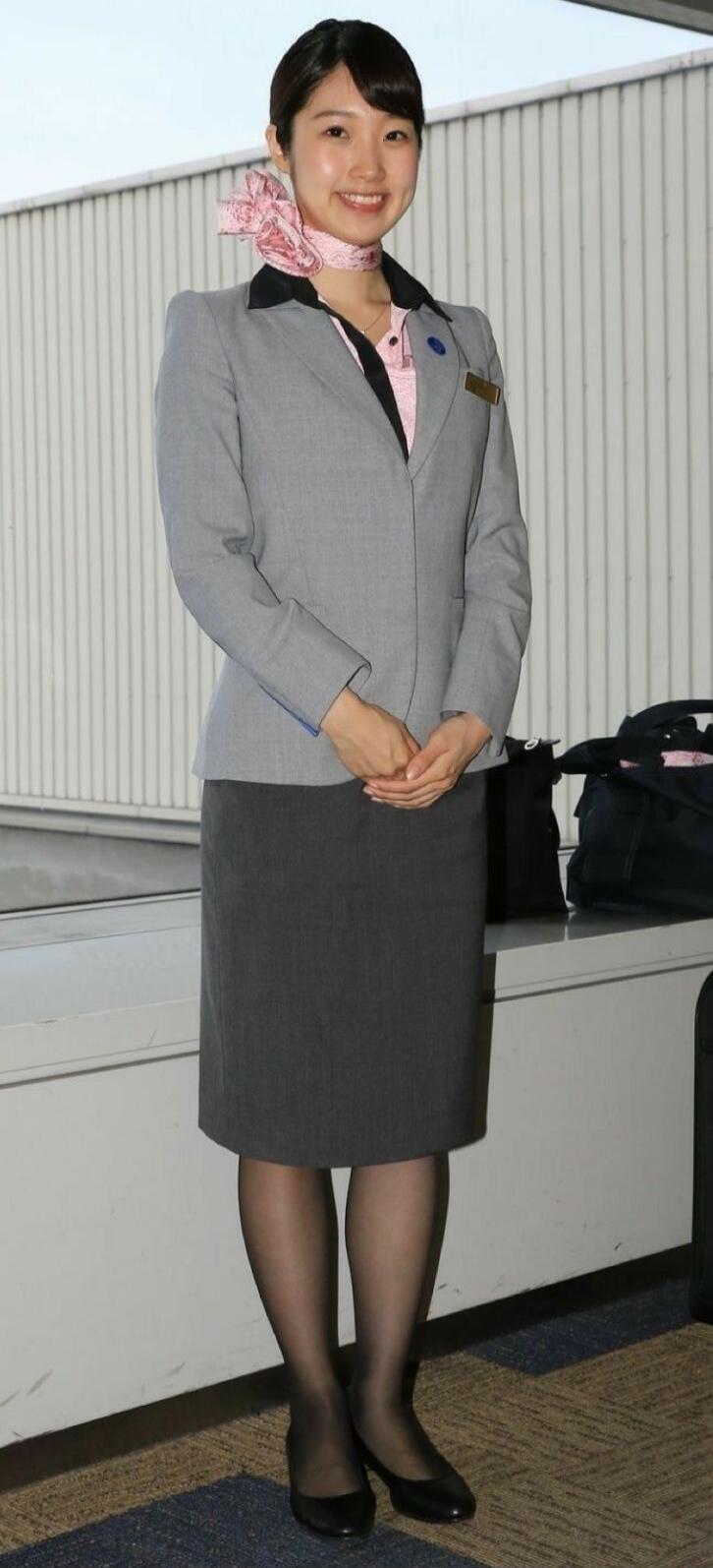 A young Asian woman in a professional uniform is smiling and standing.
