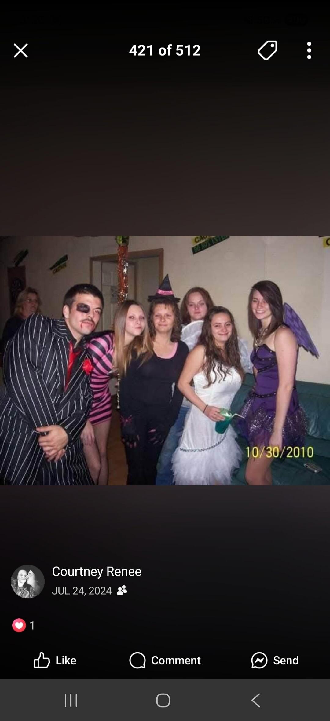 A group of people dressed in various Halloween costumes, including a man in a pinstripe suit with a painted mustache, a woman in a witch hat, and another in a purple dress with wings. One woman in a white dress holds a green drink. The date 10/30/2010 is visible on the right. Text on the wall partially reads 'CAUTION' and 'DO NOT ENTER'.